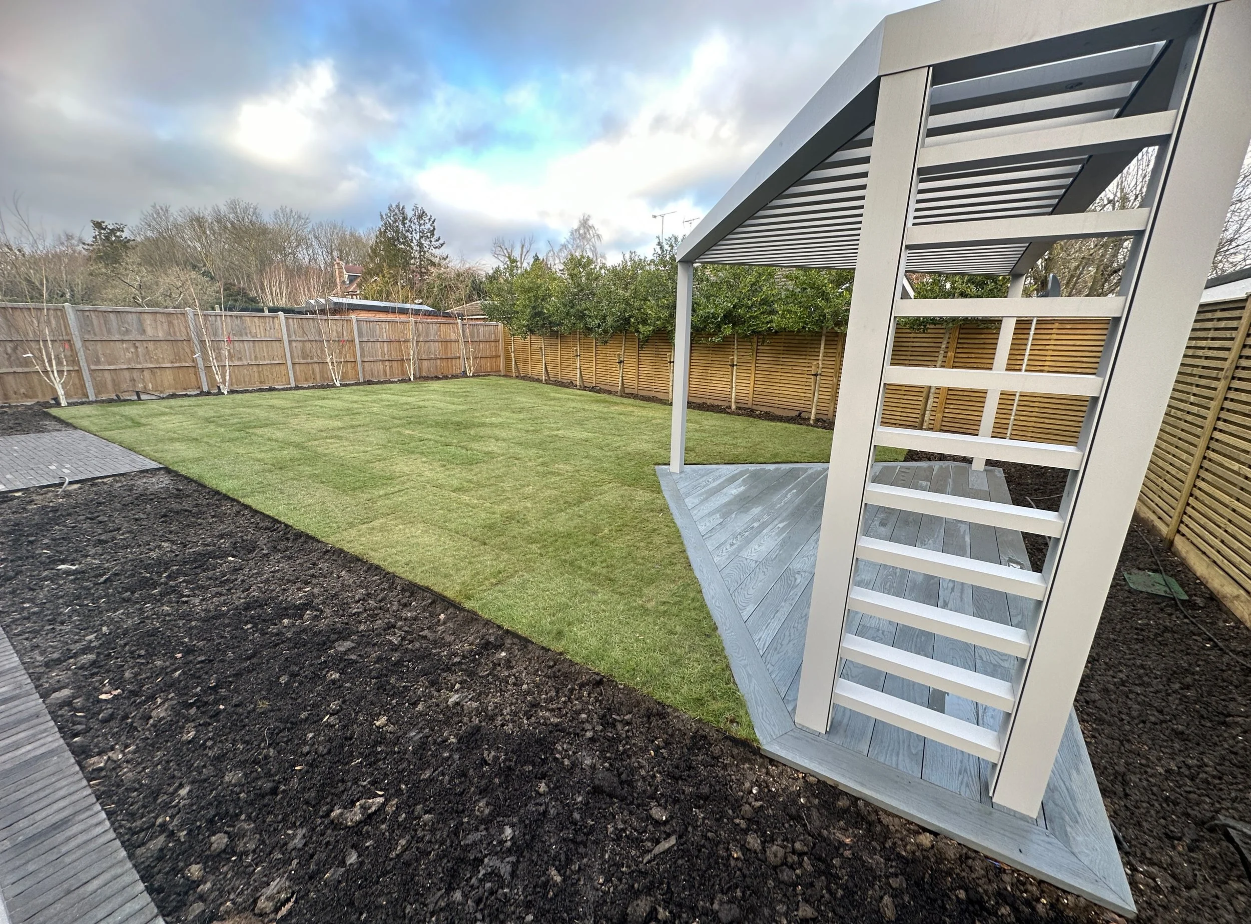 A modern backyard featuring freshly laid grass, a wooden deck, and a stylish pergola amidst a fenced area