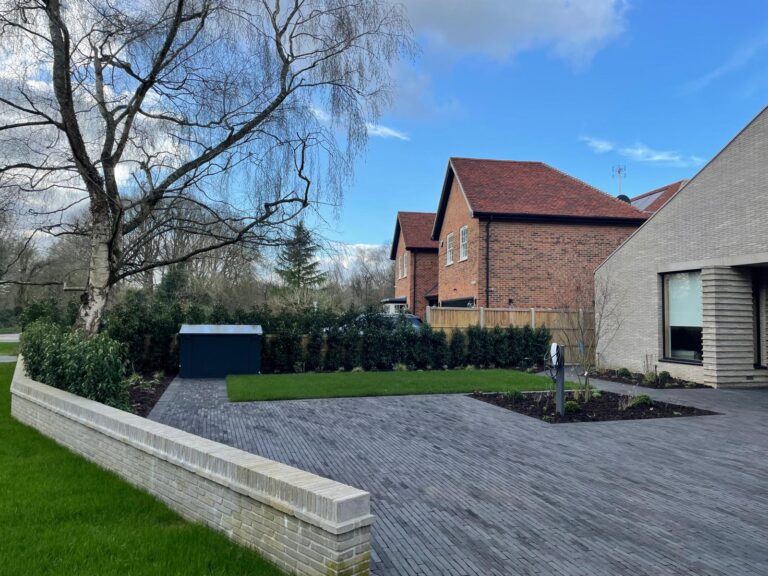 A modern residential area featuring a driveway, lush lawn, and nearby houses, framed by trees against a clear sky