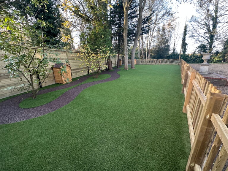Lush green artificial turf yard with winding path, wooden shed, trees, and a fenced perimeter, perfect for outdoor relaxation