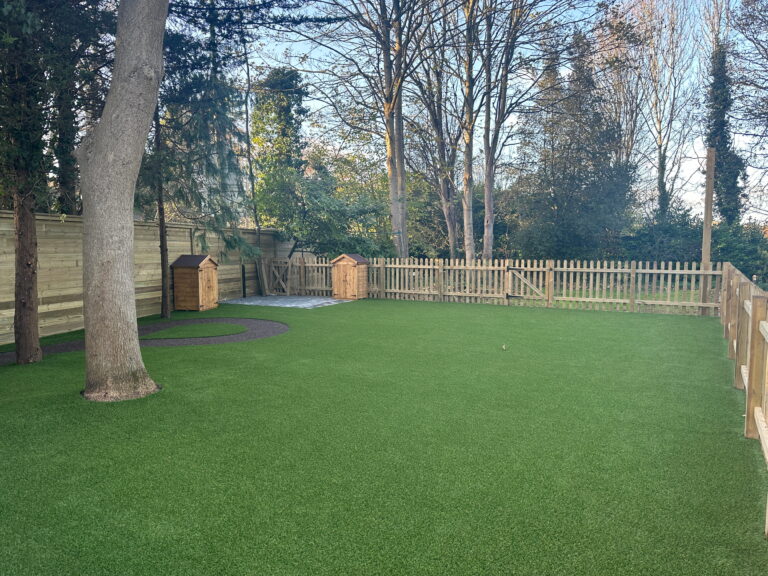 Lush green backyard with artificial turf, wooden dog houses, and a fenced area surrounded by trees, perfect for outdoor activities