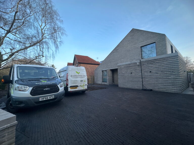 A modern house features a unique architectural design, with two work vans parked in front, on a paved driveway