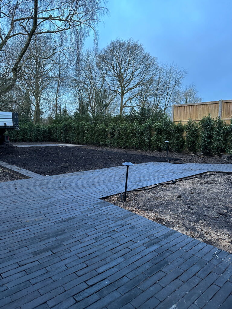A serene garden space with freshly laid dark paving, surrounded by hedges and bare trees under a blue sky