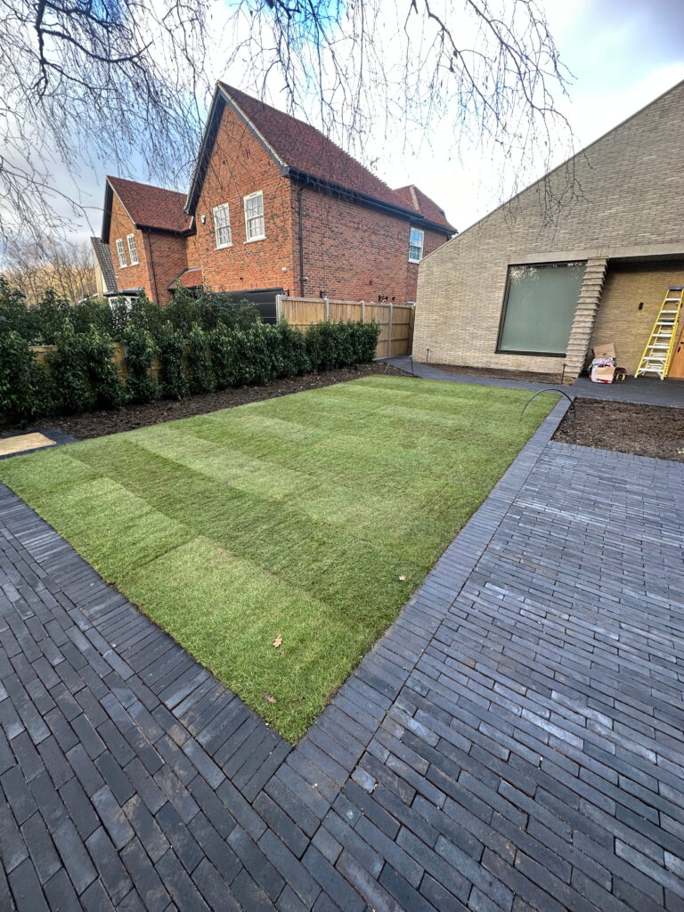 A well-maintained garden with freshly laid grass patches, surrounded by brick pathways and modern architecture