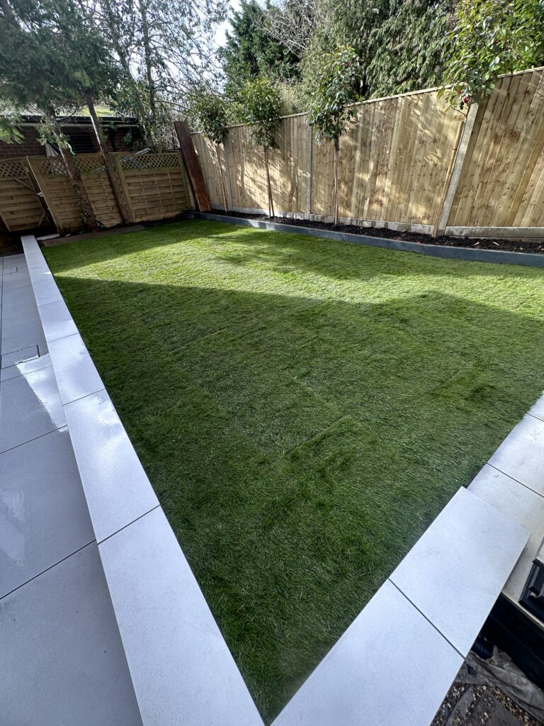 Lush green artificial turf surrounded by sleek gray paving stones and a wooden fence, perfect for outdoor relaxation