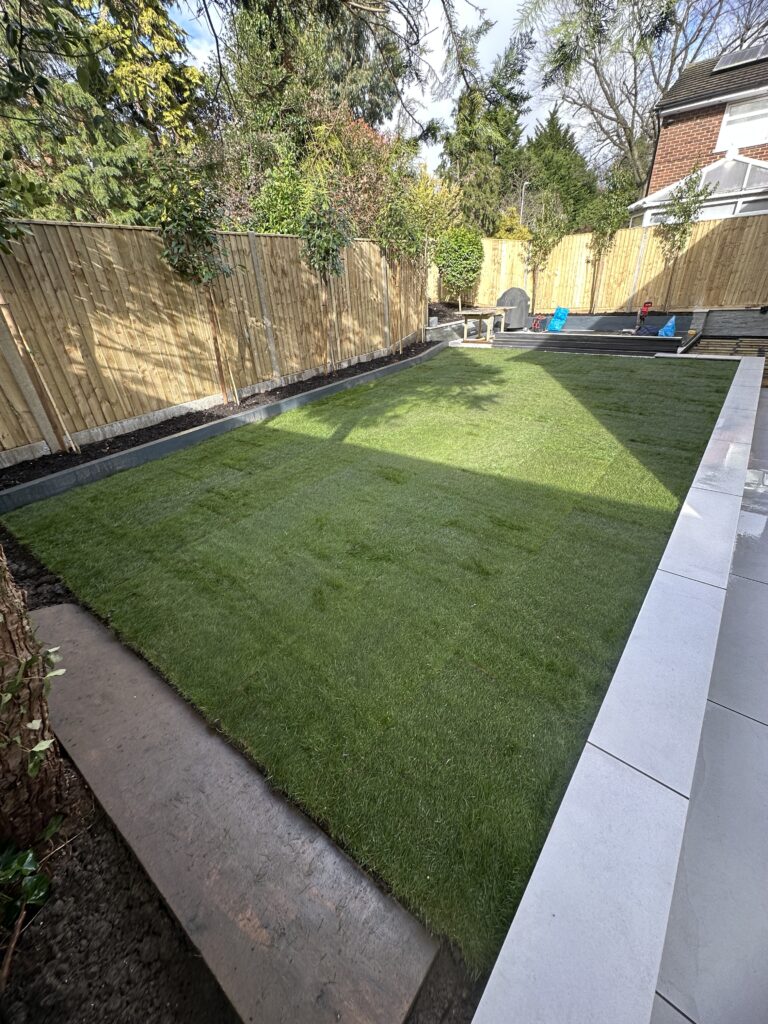 Lush green lawn bordered by wooden fencing, featuring sleek patio edges and surrounding greenery for a serene outdoor space