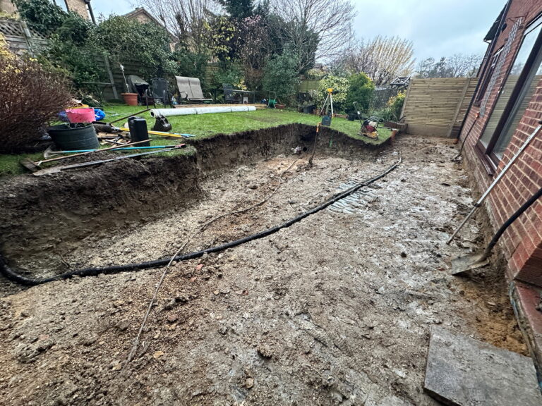 A garden under excavation, with disturbed soil, gardening tools, and a partially visible lawn area in the background