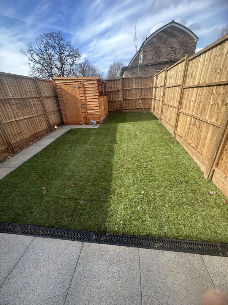 Lush green lawn with wooden shed, surrounded by wooden fencing and a clear blue sky, perfect for outdoor relaxation