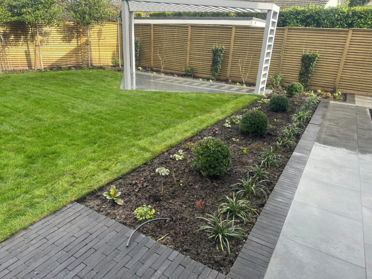 The image showcases a landscaped garden featuring lush green grass, a seating area with gray tiles, and neatly arranged flower beds
