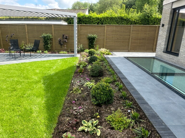 A beautifully landscaped garden featuring vibrant green grass, elegant planters, a pool, and seating area under a pergola