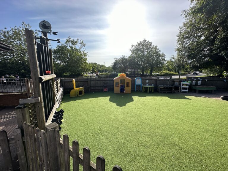A bright outdoor playground with artificial grass, colorful playhouses, and trees under a clear blue sky