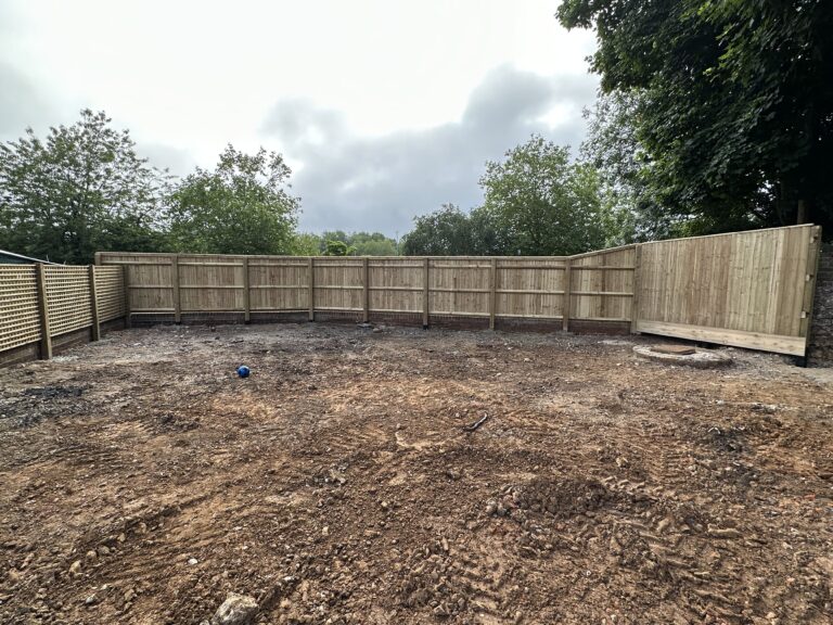 A fenced outdoor space with bare ground and a blue ball, surrounded by trees and cloudy skies