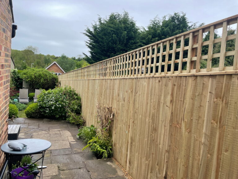 Beautiful garden scene featuring a wooden fence, lush greenery, and a cozy paved patio with outdoor furniture