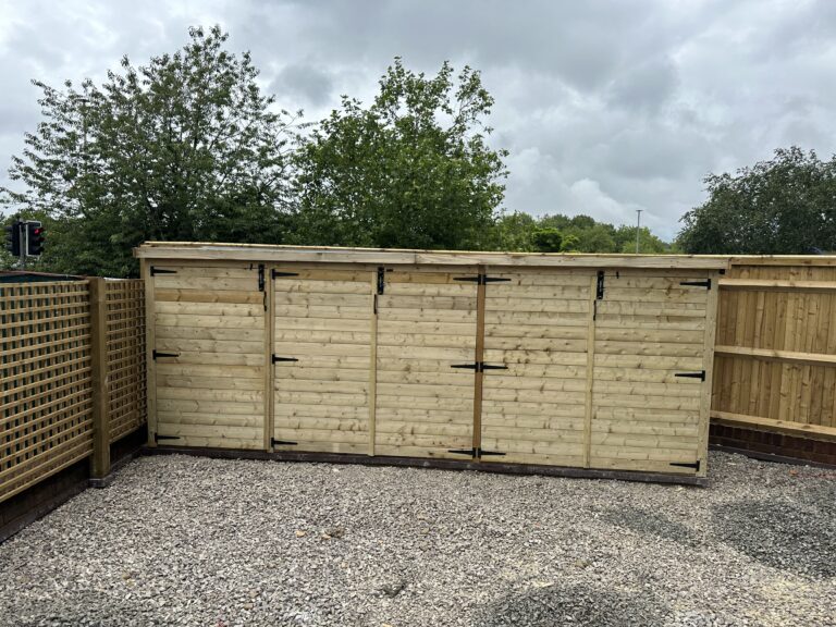 A wooden storage shed with multiple doors, set against a backdrop of trees and a cloudy sky