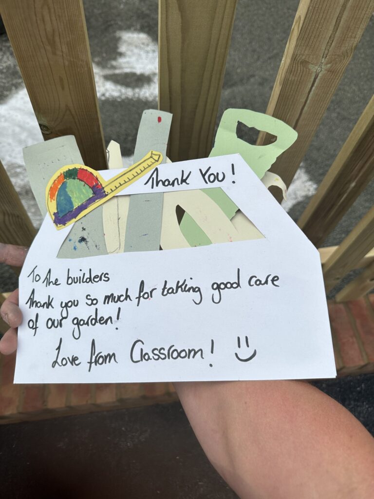 A colorful thank-you card made of cut paper, expressing gratitude to builders for garden care, held by a hand