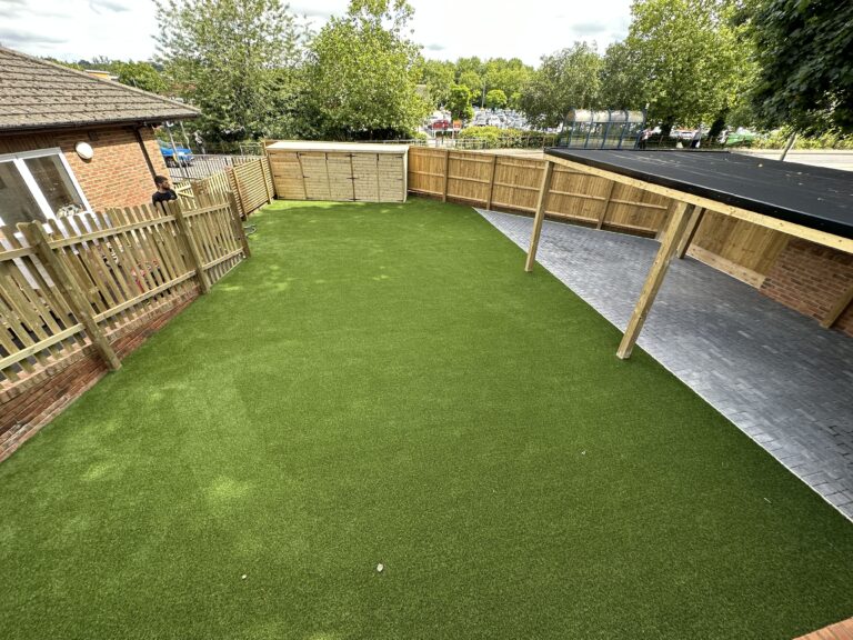 A lush green lawn with artificial turf, bordered by wooden fencing and a covered paved area, creates a cozy outdoor space