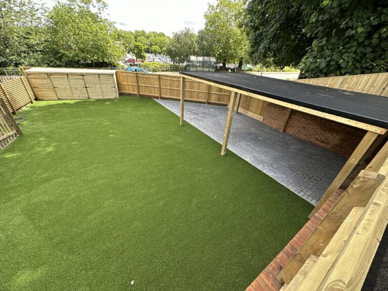 A spacious outdoor area featuring synthetic grass, wooden fencing, and a covered section with a paved surface