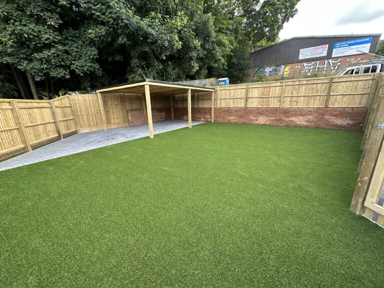 A well-maintained outdoor space features artificial grass, a wooden fence, and a covered area for shade