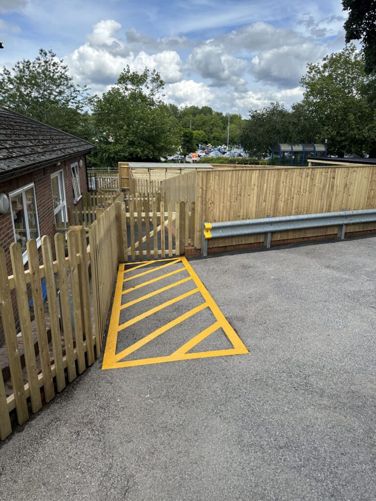 The image features a wooden fence with a yellow-striped ramp leading toward an outdoor area, surrounded by greenery and a cloudy sky