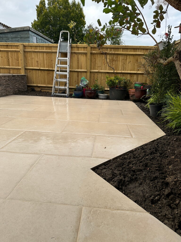 A modern patio with tiled flooring, potted plants, a ladder, and a wooden fence in the background
