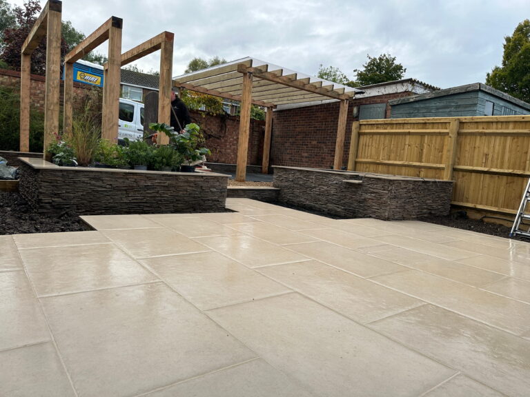A landscaped garden features a stone patio, wooden pergola, and raised plant beds, showcasing a modern outdoor space