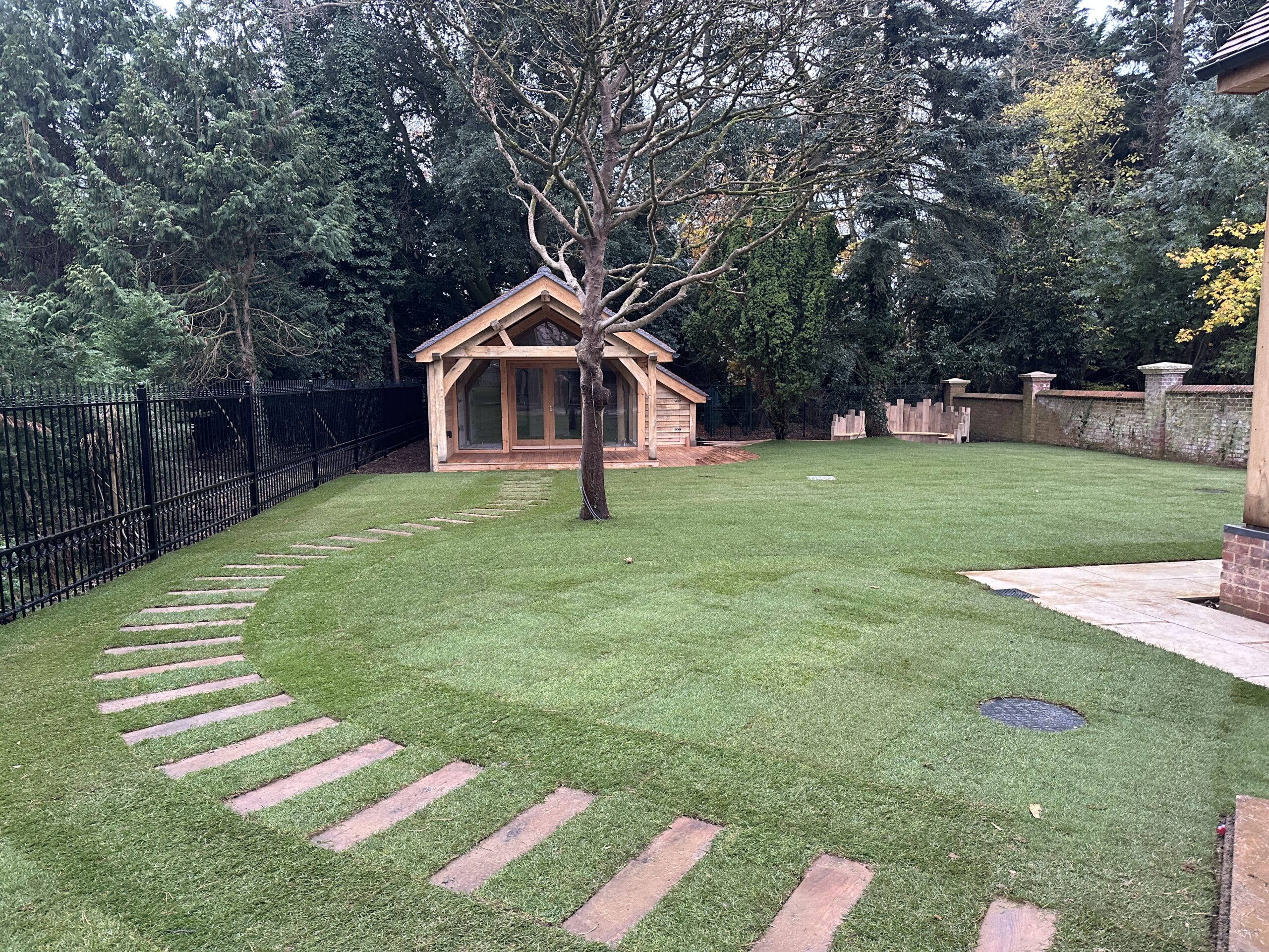 Lush garden featuring a quaint wooden cabin, curved stone path, and vibrant greenery surrounded by tall trees