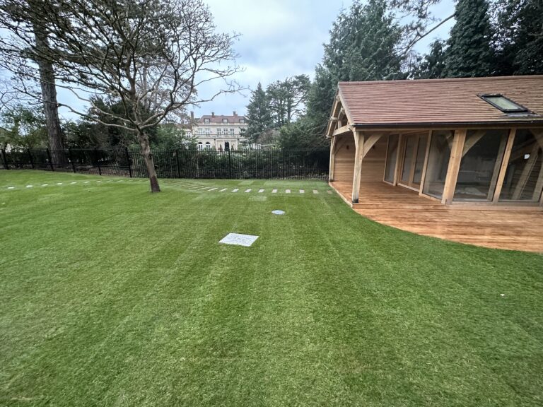 Lush green lawn with stone pathways, a wooden garden building, and a backdrop of elegant architecture and trees
