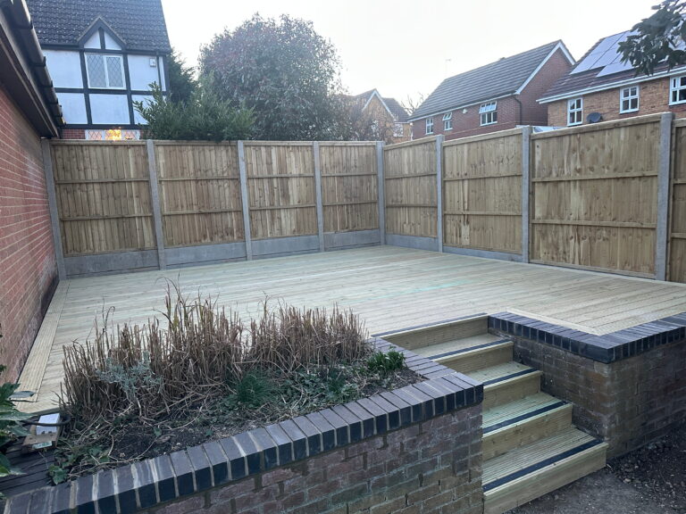Spacious wooden deck surrounded by wooden fencing, with brick steps leading to a landscaped garden in a residential area