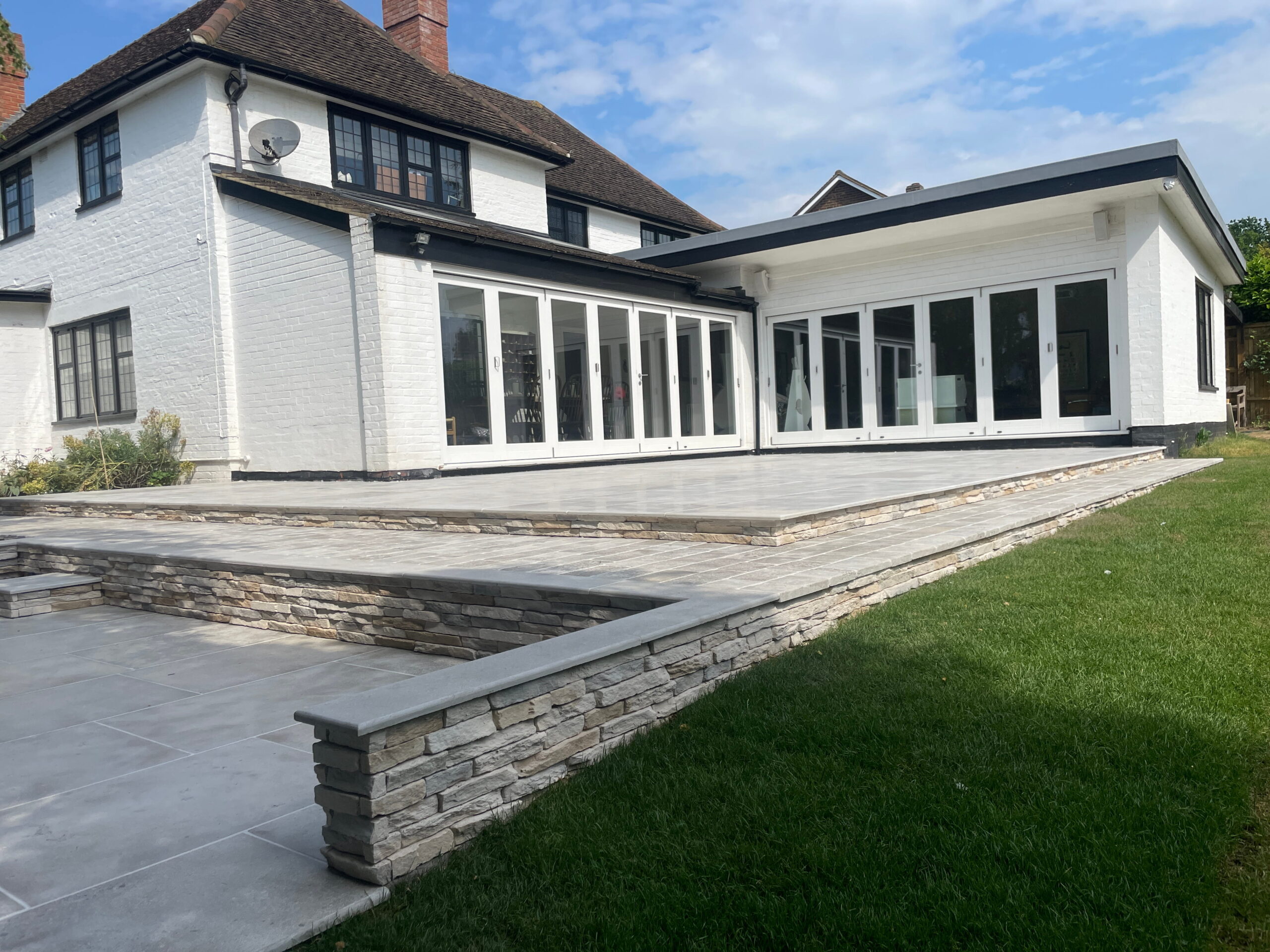 Modern white house with a stone patio, large glass doors, and a spacious lawn under a clear blue sky
