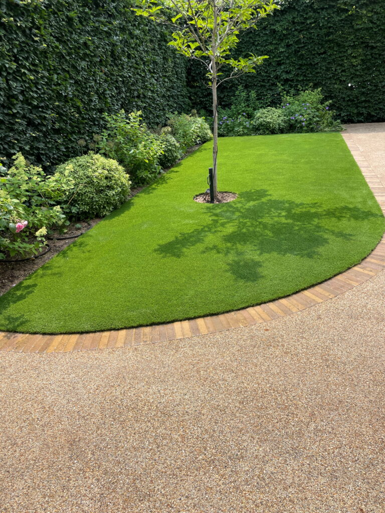 Lush green lawn surrounded by vibrant shrubs and a tree, bordered by a textured gravel pathway. Perfect garden oasis