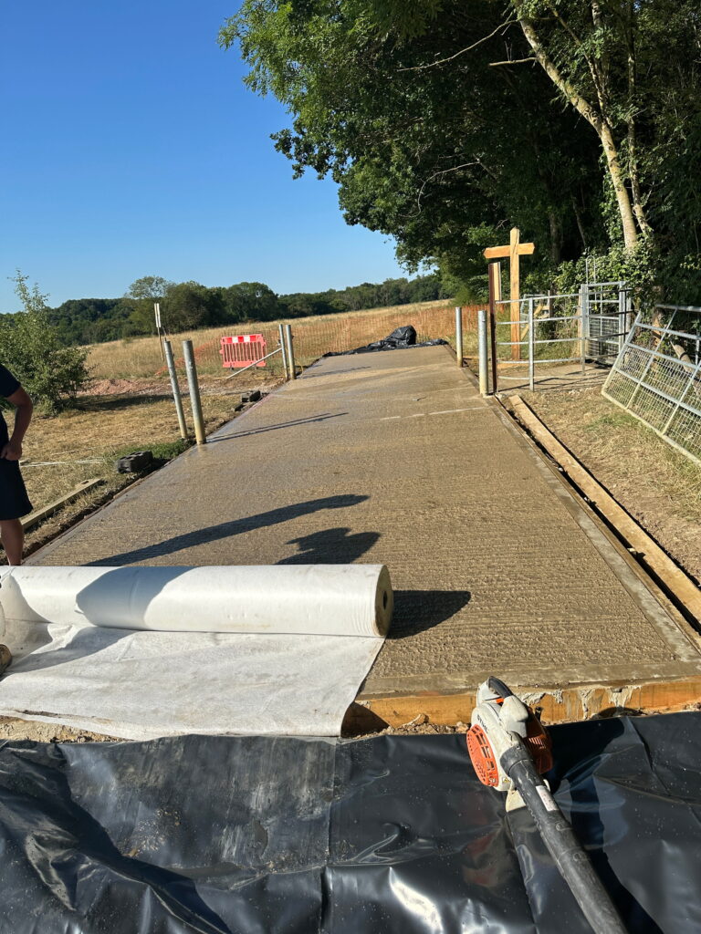 A freshly poured concrete pathway stretches through a green area, with construction materials and equipment visible