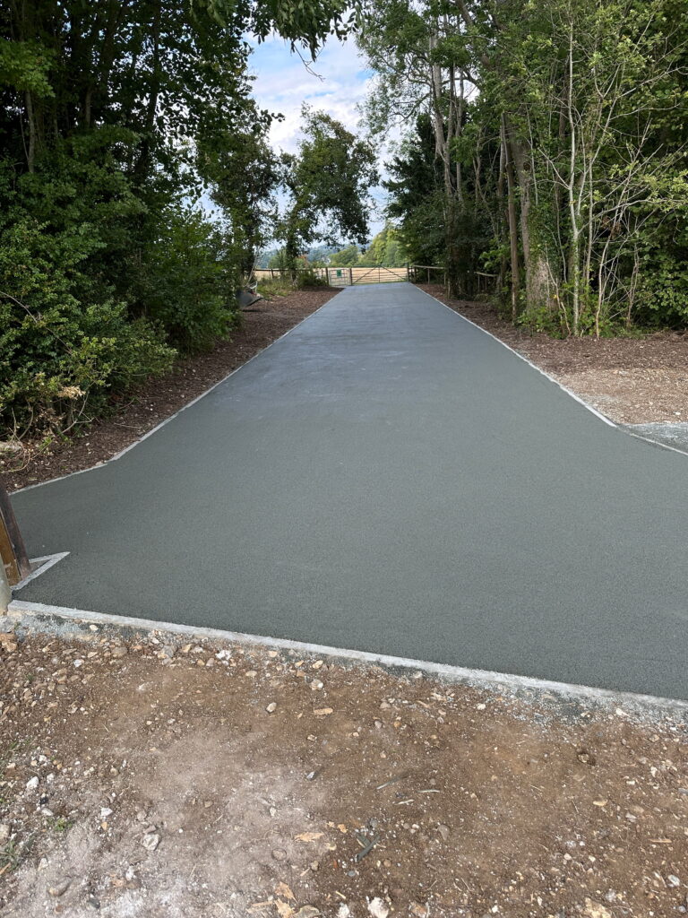 A freshly paved path surrounded by trees leads to a gate, providing access to an open area