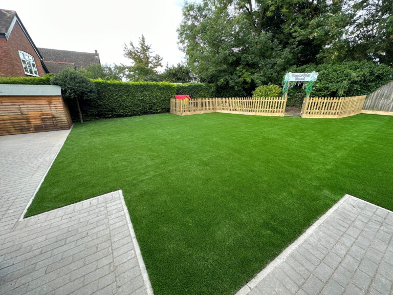 Lush green artificial lawn beside a patio, wooden fence, and children's playhouse, creating a vibrant outdoor space