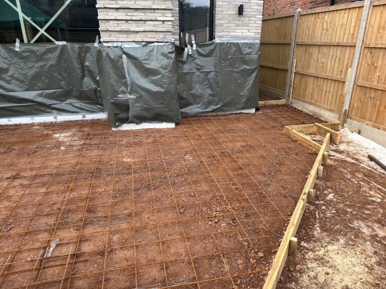 The image shows a construction site with exposed soil and a wire mesh foundation, covered partially with plastic sheeting