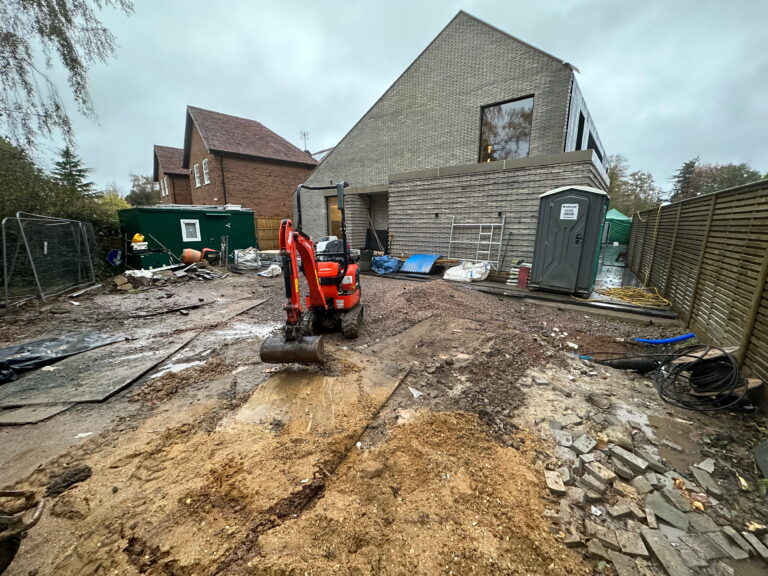 A construction site with a mini excavator, piles of materials, and a partially built house under a cloudy sky