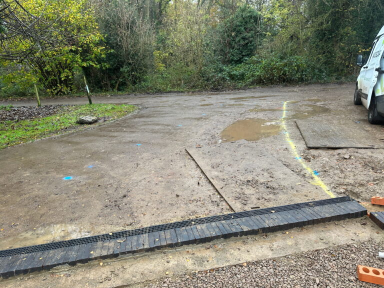 A muddy area with patches of standing water, marked with blue and yellow lines, and a parked van nearby