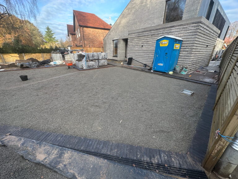 A construction site features a gravel area, a portable restroom, and stacked materials near a modern building under development