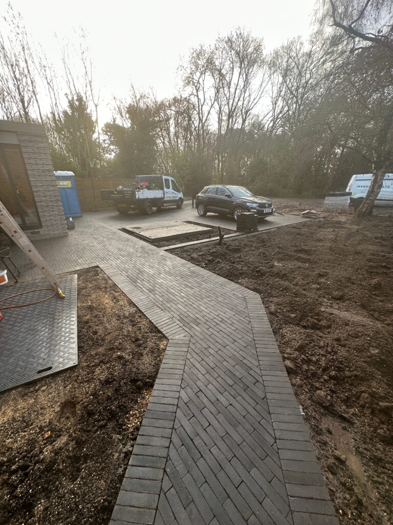 A newly paved pathway curves through a construction site with vehicles and unfinished landscaping. Trees are visible in the background