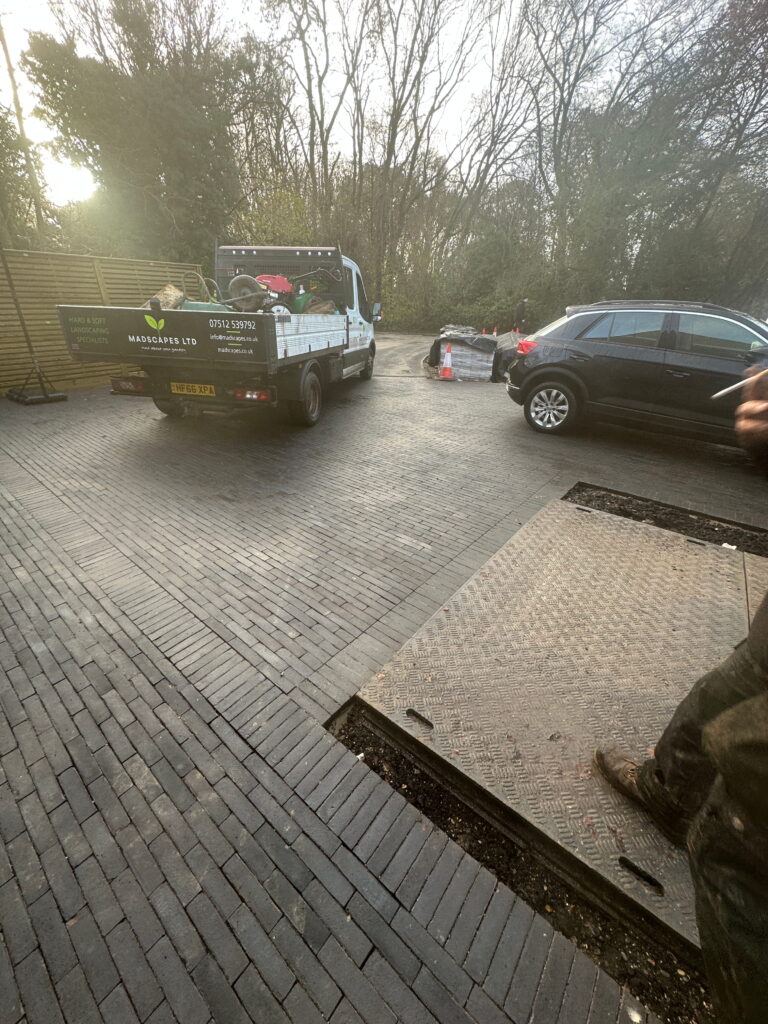 A truck is parked on a brick driveway surrounded by trees, with landscaping equipment visible in the back