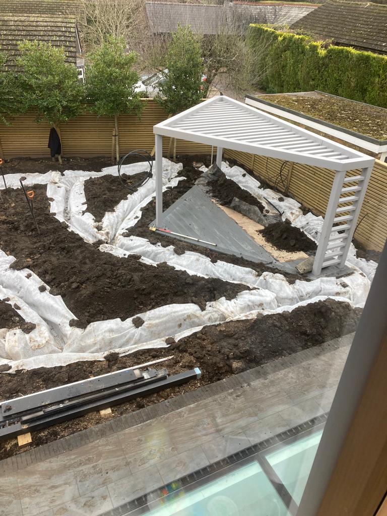 The image shows a construction site with soil mounds, a white tarp, and a modern gazebo structure being built