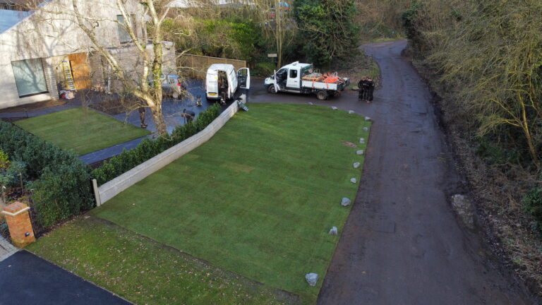 A modern house with two vehicles parked outside, featuring freshly laid lawns and surrounding trees