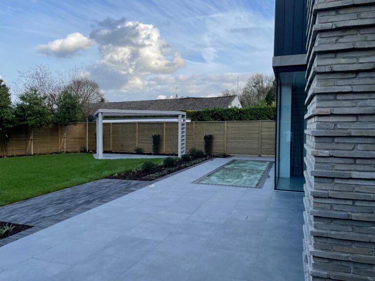 A modern outdoor space featuring a manicured lawn, sleek patio, and a cozy pergola, framed by lush greenery