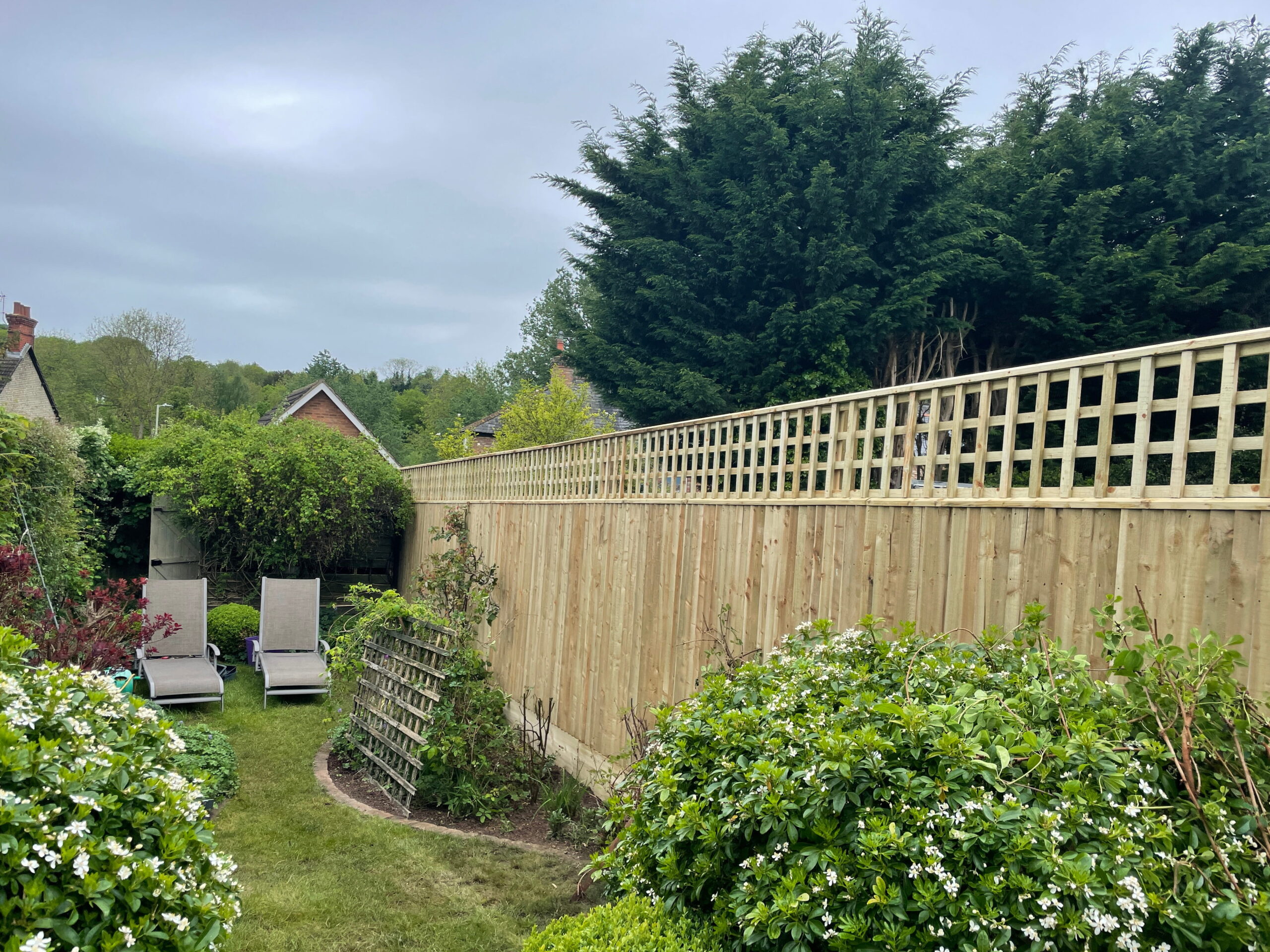 Lush garden featuring wooden fencing, relaxing loungers, and vibrant greenery under overcast skies for tranquil outdoor spaces
