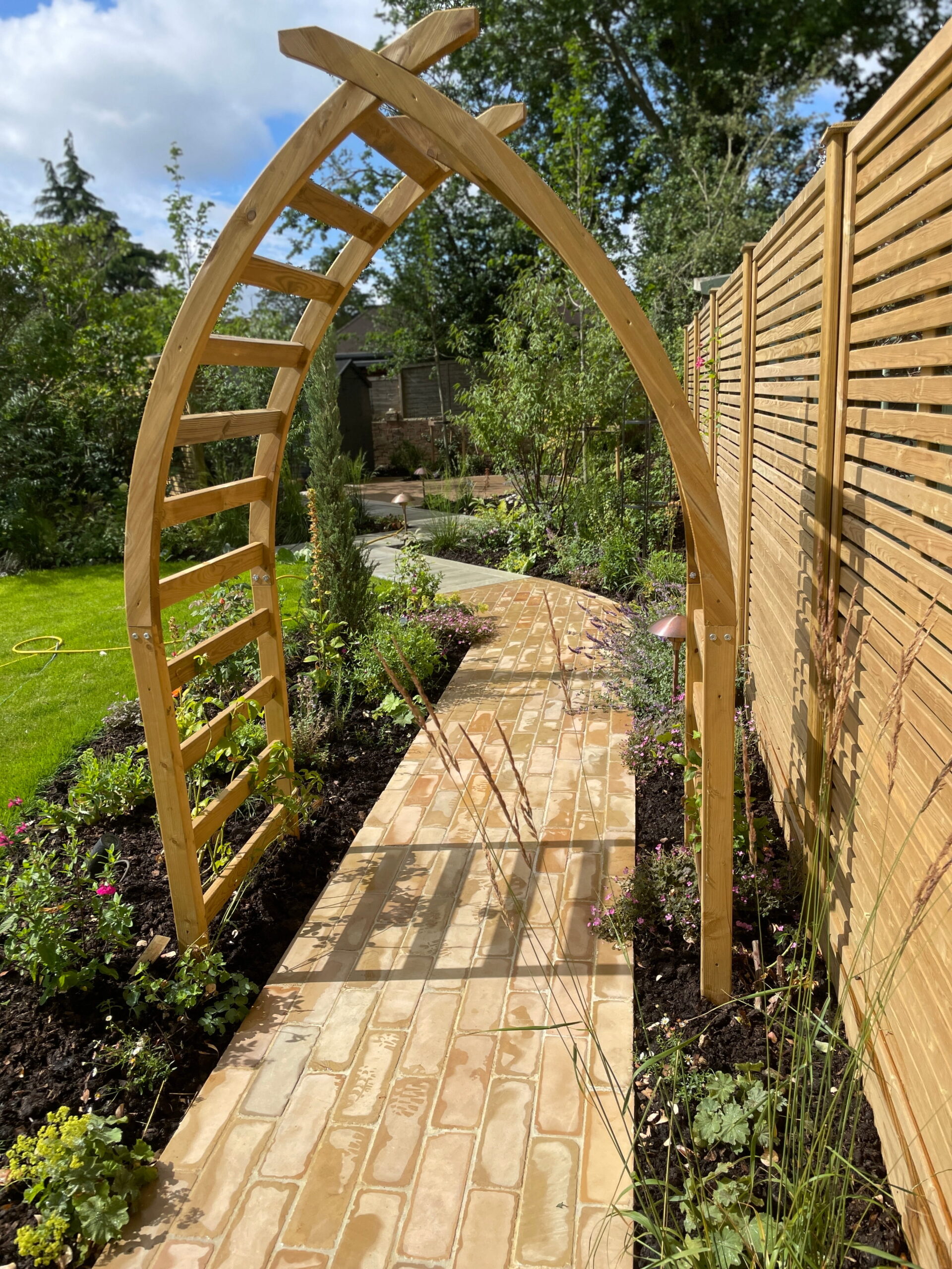 A wooden archway over a garden path lined with flowers and greenery.