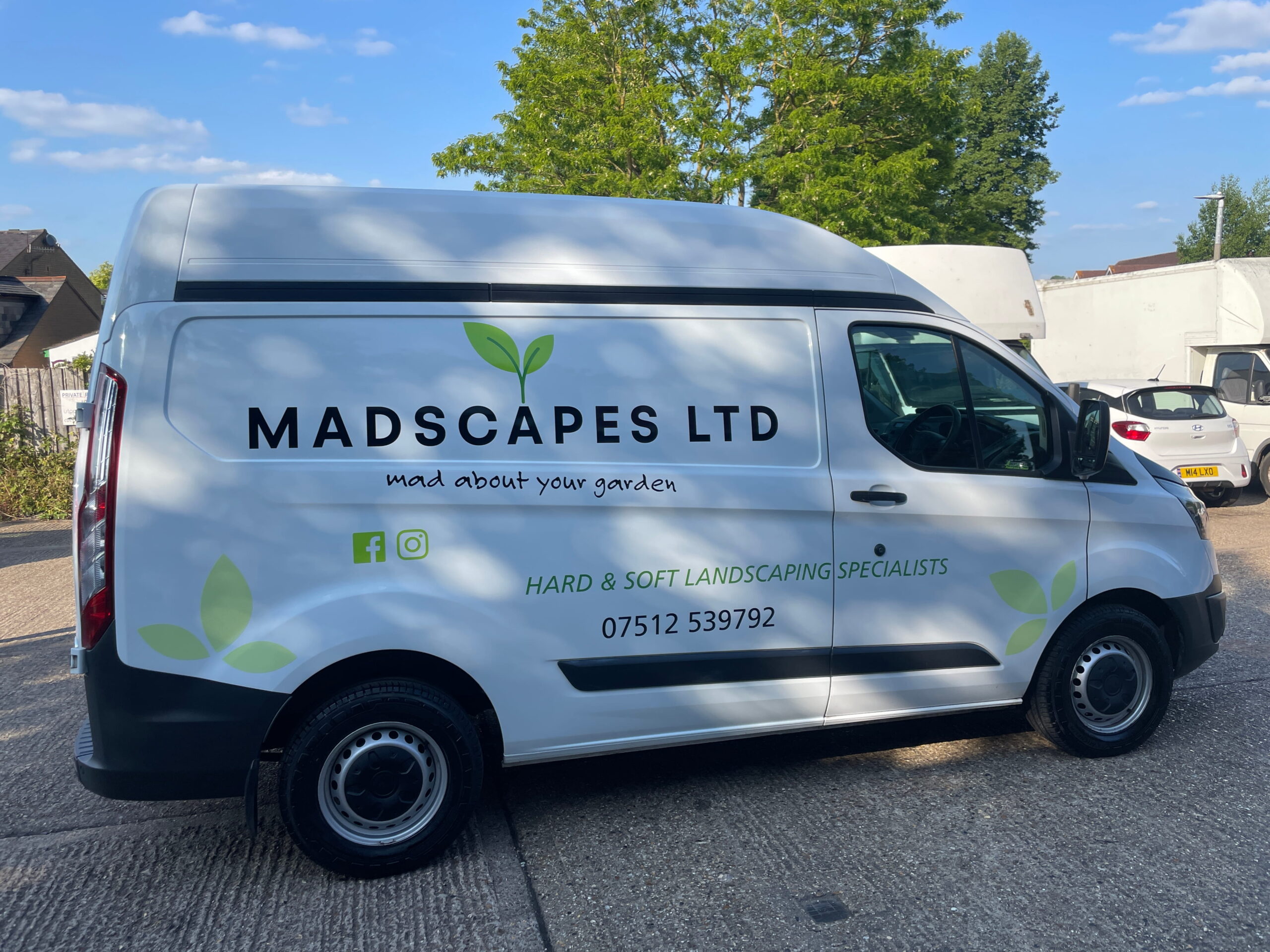 White van for Madscapes Ltd, landscaping specialists, parked in a green outdoor area with trees under a clear blue sky